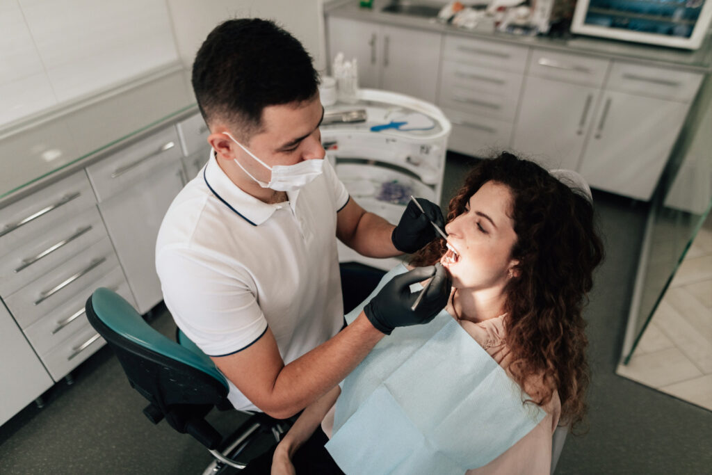 A dentist conducting a check-up on a patient, with the patient reclined in a dental chair while the dentist examines their teeth.