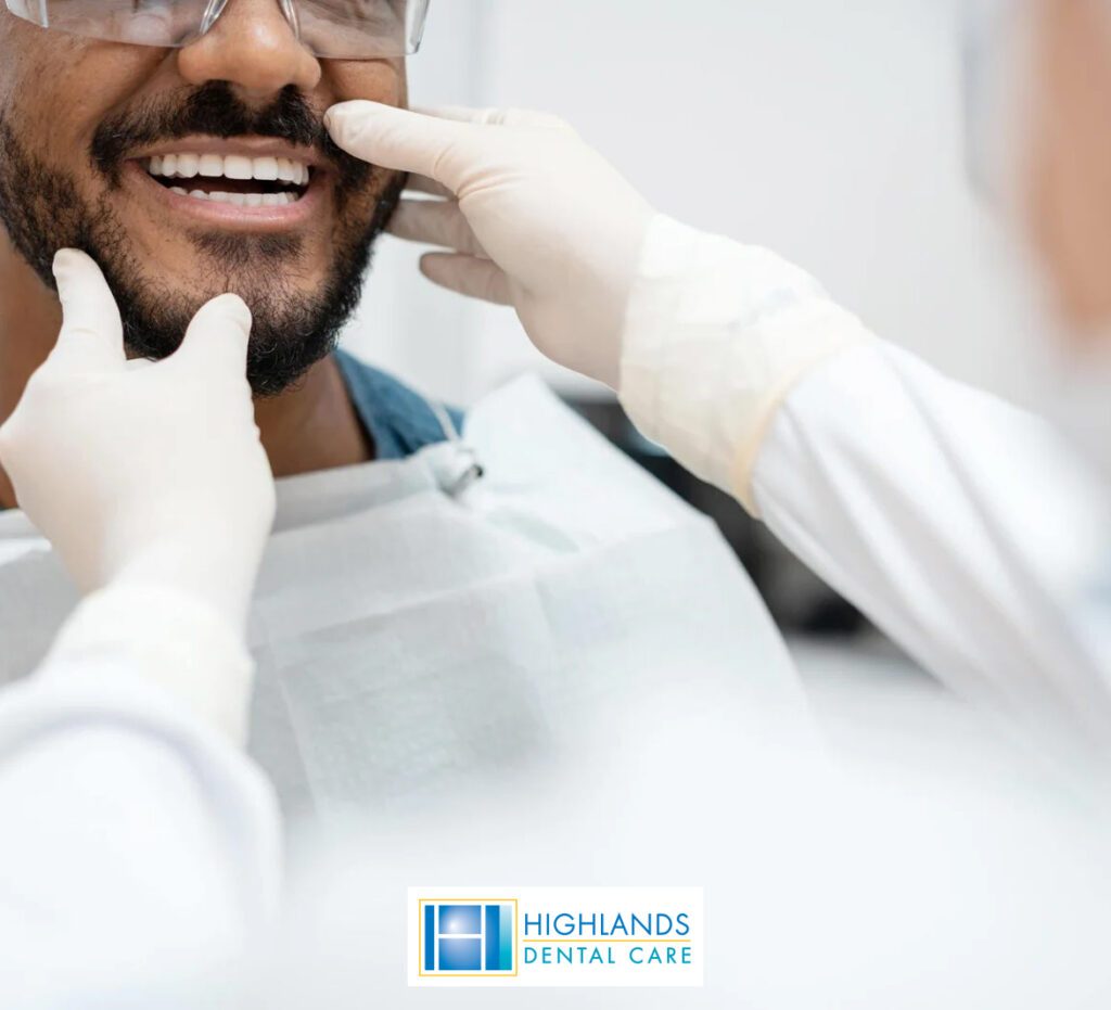 A dentist examining a patient's mouth, using gloved hands to touch and inspect the teeth and gums.